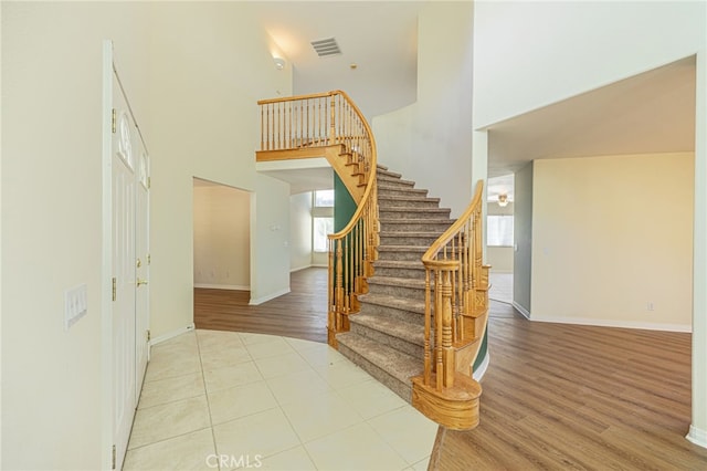 staircase featuring visible vents, wood finished floors, a towering ceiling, and baseboards