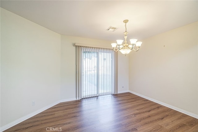 unfurnished room featuring a notable chandelier, wood finished floors, visible vents, and baseboards