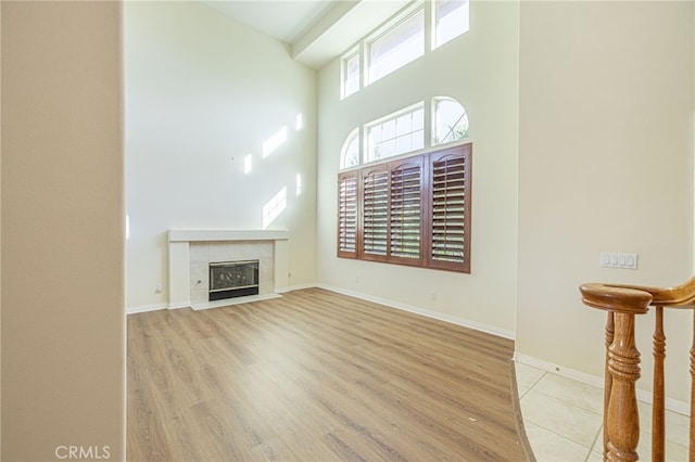 unfurnished living room with baseboards, a tile fireplace, a towering ceiling, and light wood-style floors