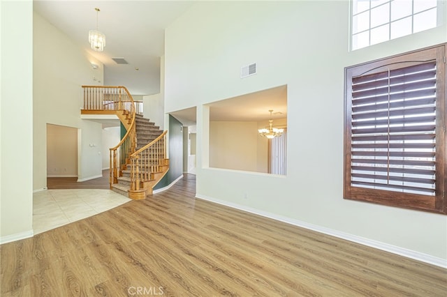 unfurnished living room featuring stairway, visible vents, a chandelier, and wood finished floors