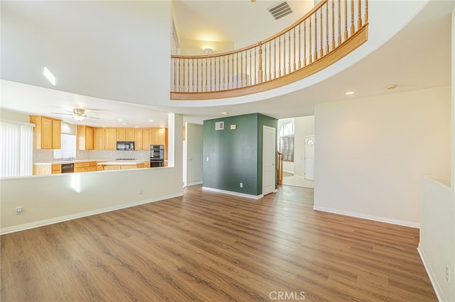 unfurnished living room featuring a high ceiling, visible vents, baseboards, and wood finished floors