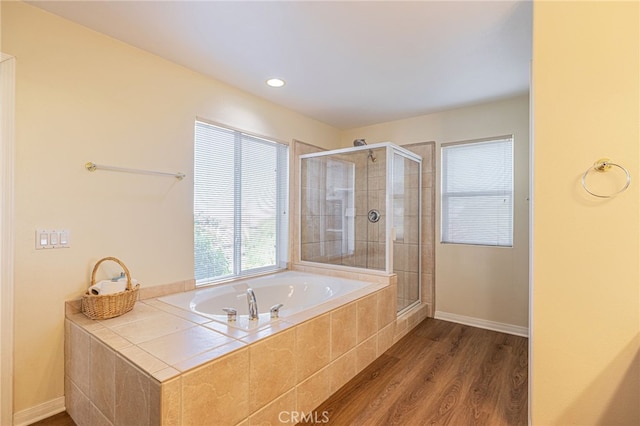 full bath featuring a bath, a stall shower, baseboards, and wood finished floors