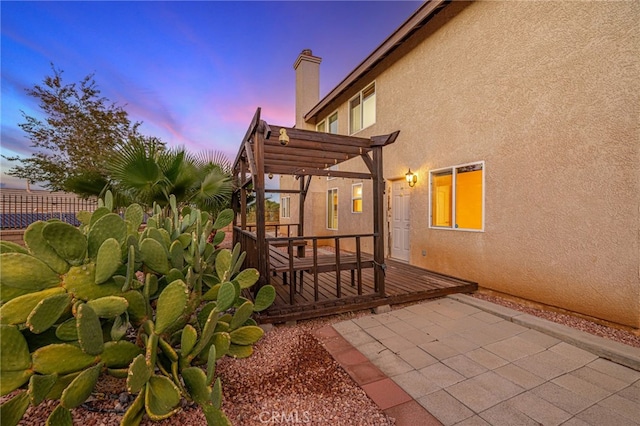 view of property exterior with a chimney, stucco siding, fence, a pergola, and a wooden deck