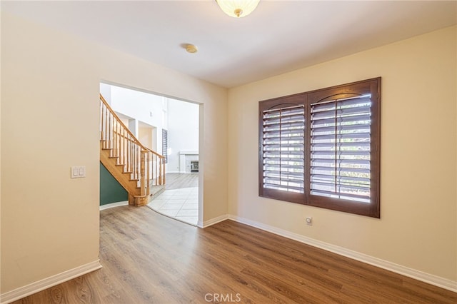 unfurnished room with baseboards, a fireplace, stairway, and wood finished floors