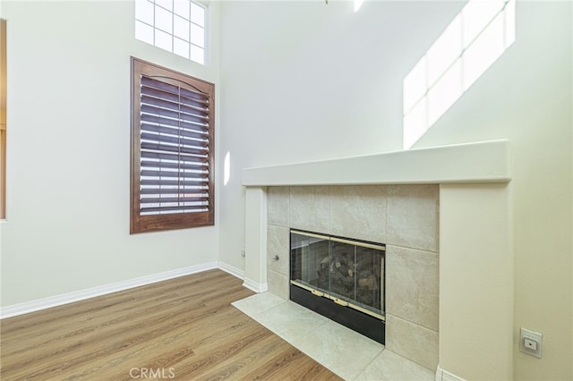 unfurnished living room featuring a wealth of natural light, a tiled fireplace, baseboards, and wood finished floors