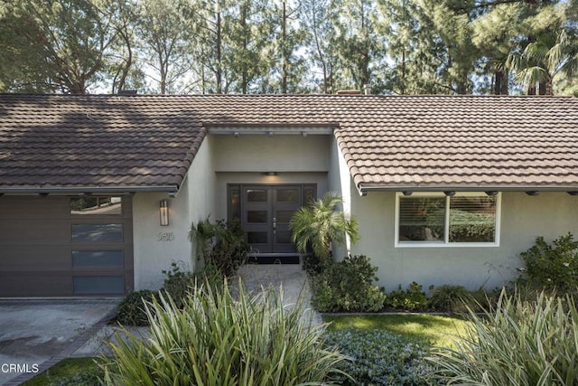 entrance to property featuring a garage, french doors, a tiled roof, and stucco siding