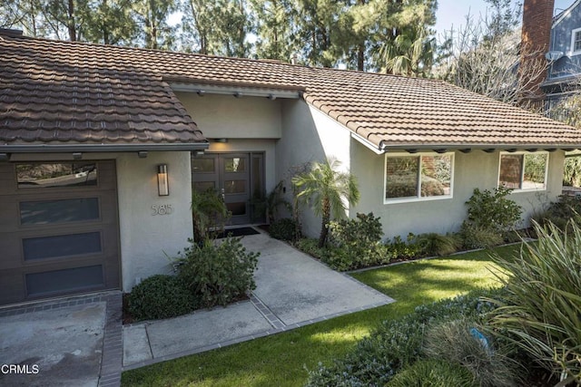 entrance to property with a yard, an attached garage, and stucco siding