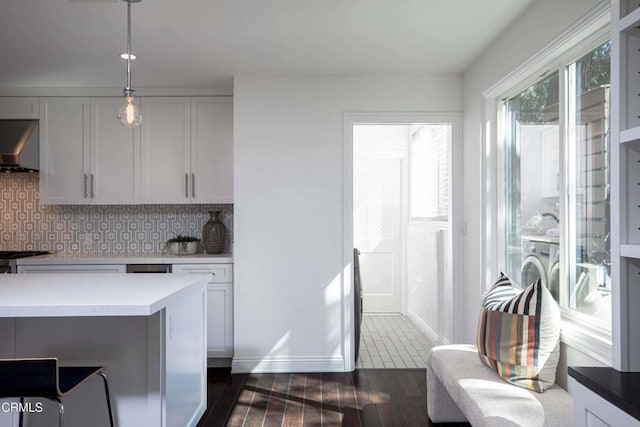 kitchen featuring dark wood-style floors, decorative light fixtures, light countertops, decorative backsplash, and wall chimney exhaust hood