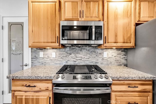 kitchen with appliances with stainless steel finishes, light brown cabinets, backsplash, and light stone counters