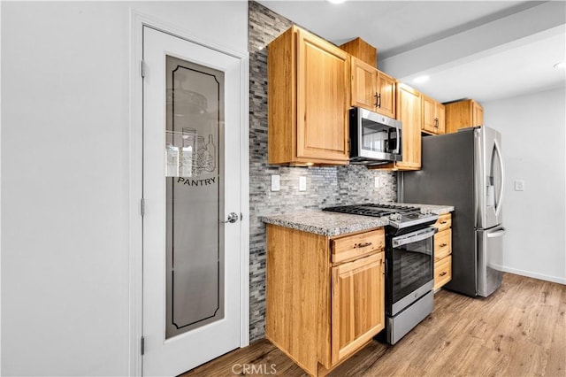 kitchen with light stone counters, light wood-style flooring, stainless steel appliances, baseboards, and backsplash