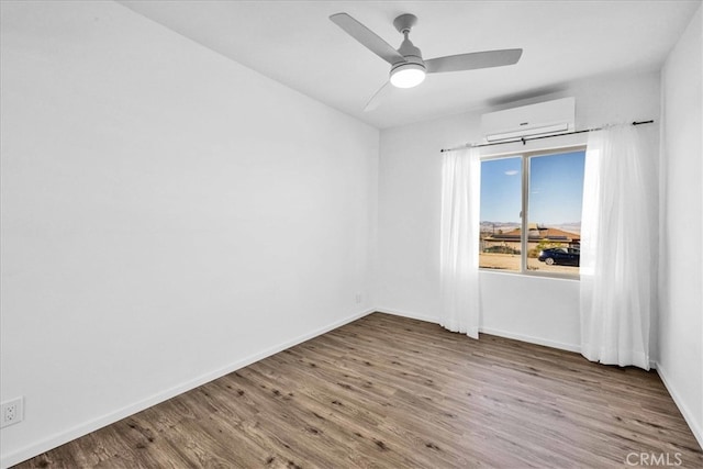 empty room with a wall unit AC, ceiling fan, baseboards, and wood finished floors