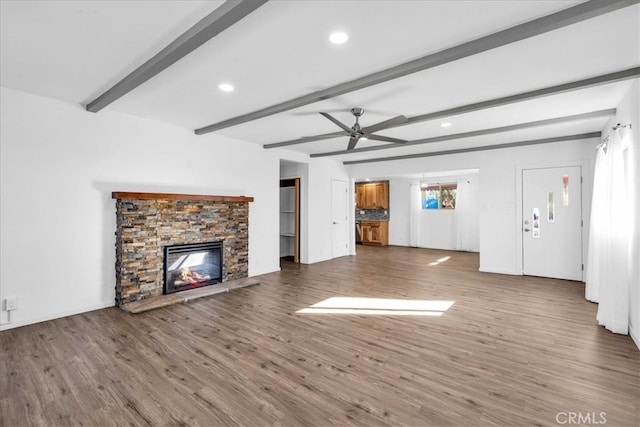 unfurnished living room with beam ceiling, a ceiling fan, wood finished floors, and a stone fireplace