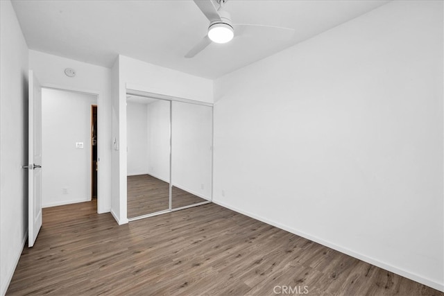 unfurnished bedroom with a closet, wood finished floors, a ceiling fan, and baseboards