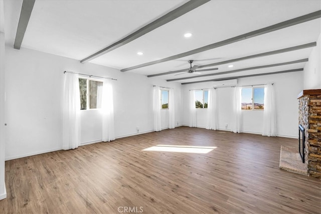 unfurnished living room with a wealth of natural light, a stone fireplace, a wall unit AC, and beam ceiling