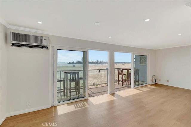 unfurnished room featuring baseboards, a wall mounted AC, wood finished floors, and crown molding