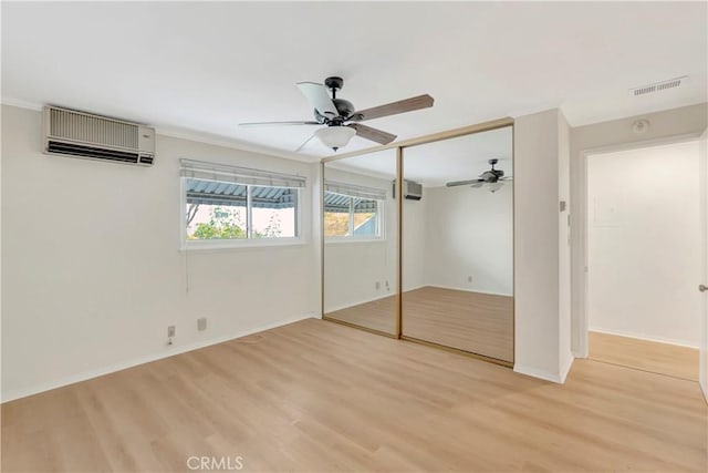 unfurnished bedroom with a wall unit AC, a ceiling fan, visible vents, light wood-style floors, and a closet