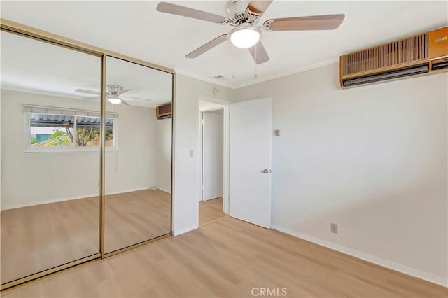 unfurnished bedroom featuring light wood-style flooring, a closet, crown molding, and an AC wall unit