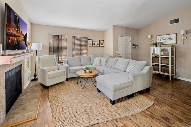 living area featuring a fireplace, lofted ceiling, visible vents, wood finished floors, and baseboards