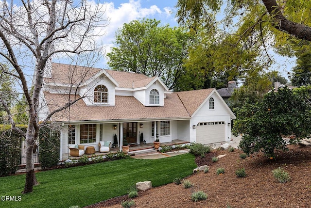 view of front of house with an attached garage, covered porch, a shingled roof, and a front yard