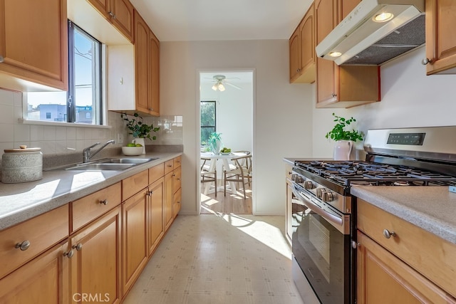 kitchen with plenty of natural light, light floors, under cabinet range hood, stainless steel range with gas cooktop, and a sink