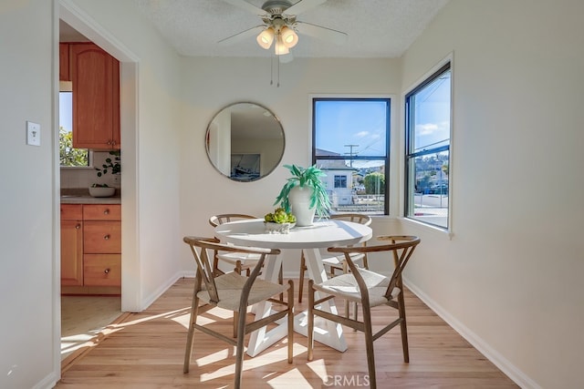 dining space with a textured ceiling, ceiling fan, light wood finished floors, and baseboards