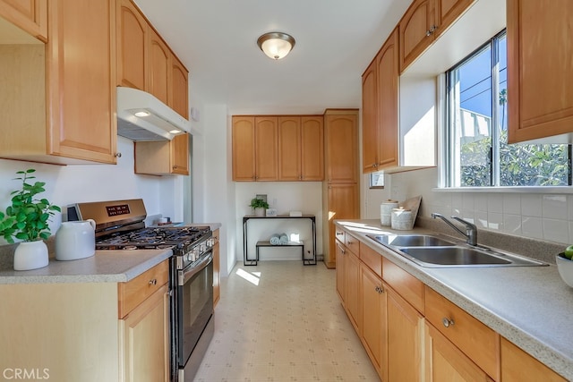 kitchen featuring stainless steel gas range oven, under cabinet range hood, a sink, light countertops, and light floors