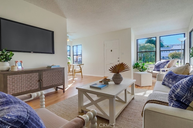 living area with a textured ceiling, baseboards, a ceiling fan, and light wood-style floors