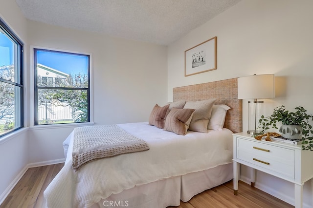 bedroom with a textured ceiling, baseboards, and light wood-style floors