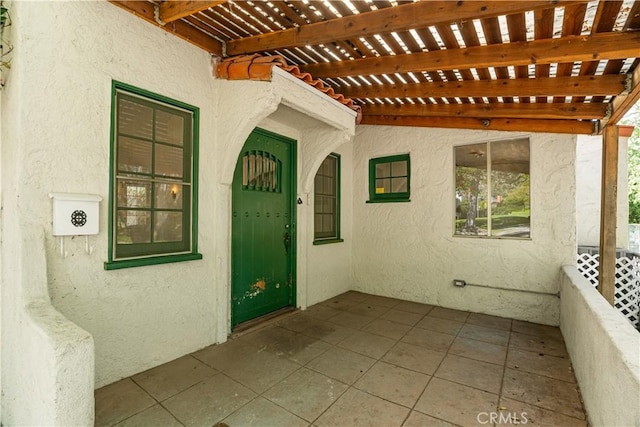 view of exterior entry featuring a patio, a pergola, and stucco siding