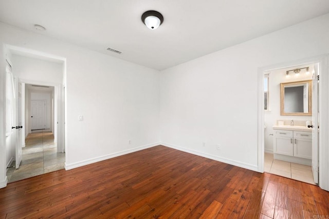 unfurnished bedroom with hardwood / wood-style flooring, a sink, visible vents, and baseboards