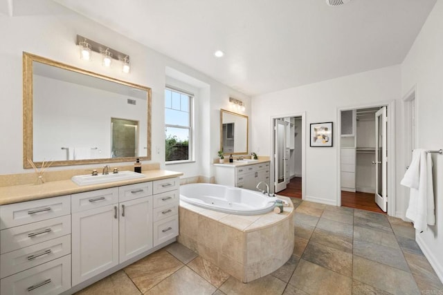 full bath with a whirlpool tub, a spacious closet, two vanities, and a sink