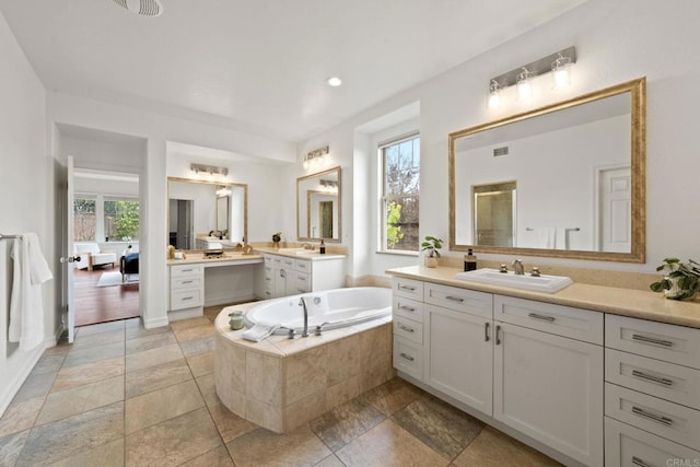 bathroom featuring two vanities, a stall shower, a garden tub, and a sink