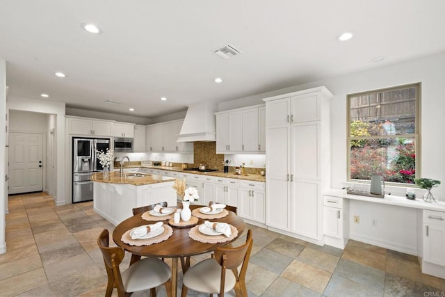 kitchen with a kitchen island with sink, a sink, visible vents, appliances with stainless steel finishes, and custom exhaust hood