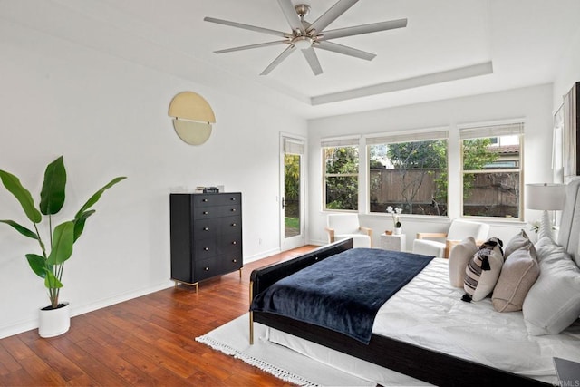 bedroom featuring wood-type flooring, a raised ceiling, a ceiling fan, and baseboards