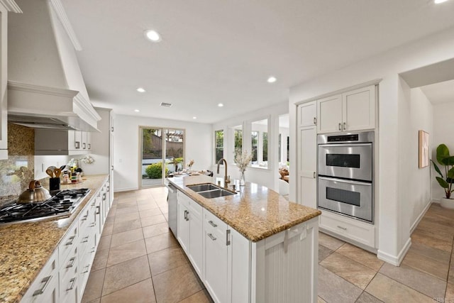 kitchen featuring custom exhaust hood, backsplash, appliances with stainless steel finishes, a sink, and an island with sink