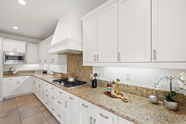 kitchen featuring premium range hood, white cabinetry, appliances with stainless steel finishes, backsplash, and light stone countertops