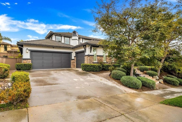 prairie-style home featuring stucco siding, an attached garage, fence, stone siding, and driveway