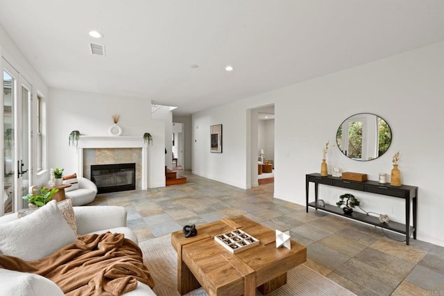 living area with a tile fireplace, recessed lighting, visible vents, baseboards, and stone finish flooring