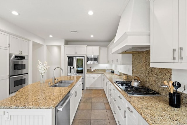 kitchen with custom range hood, appliances with stainless steel finishes, white cabinets, and a sink