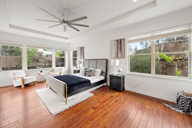 bedroom featuring a tray ceiling, wood-type flooring, and baseboards