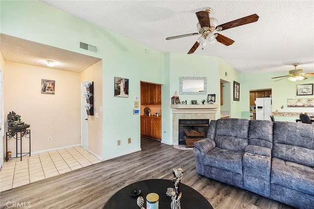 living area featuring a textured ceiling, ceiling fan, a fireplace, wood finished floors, and visible vents