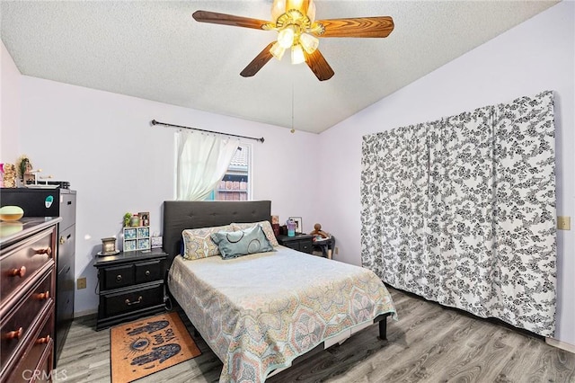 bedroom featuring light wood-type flooring, a ceiling fan, vaulted ceiling, and a textured ceiling