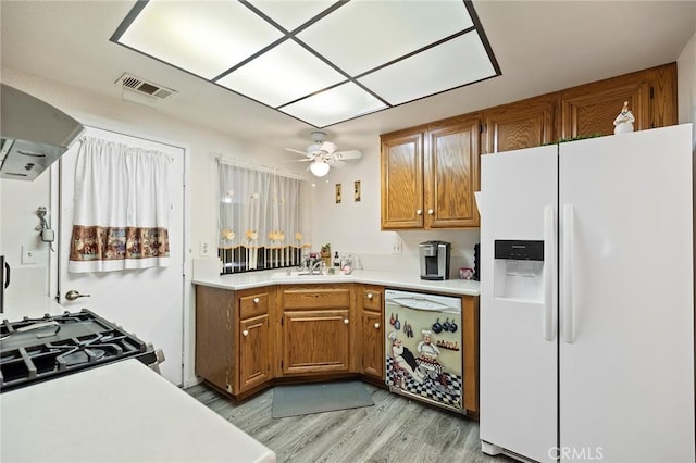 kitchen with light wood-style flooring, white appliances, light countertops, wall chimney exhaust hood, and brown cabinetry