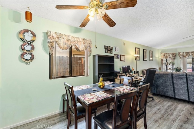 dining space with lofted ceiling, ceiling fan, a textured ceiling, wood finished floors, and baseboards