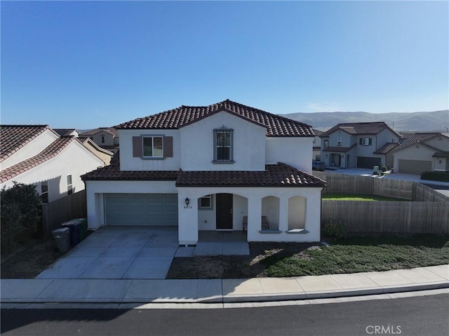 mediterranean / spanish-style home featuring driveway, a tile roof, fence, a mountain view, and stucco siding