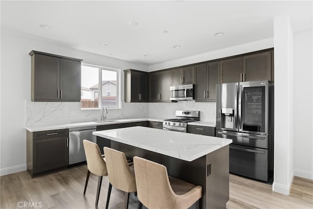 kitchen with stainless steel appliances, a kitchen island, a sink, light wood-style floors, and decorative backsplash