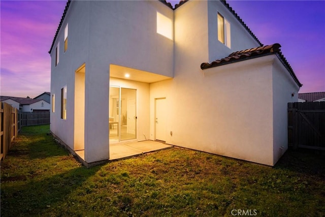 back of house at dusk with a lawn, a patio, a fenced backyard, a tiled roof, and stucco siding