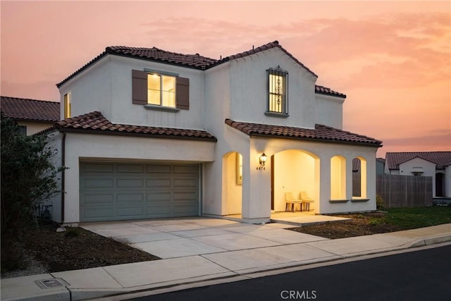 mediterranean / spanish house with a garage, fence, concrete driveway, and a tiled roof