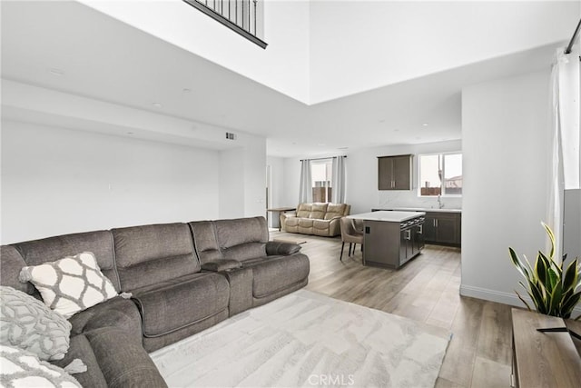 living room featuring a high ceiling, light wood-type flooring, visible vents, and baseboards