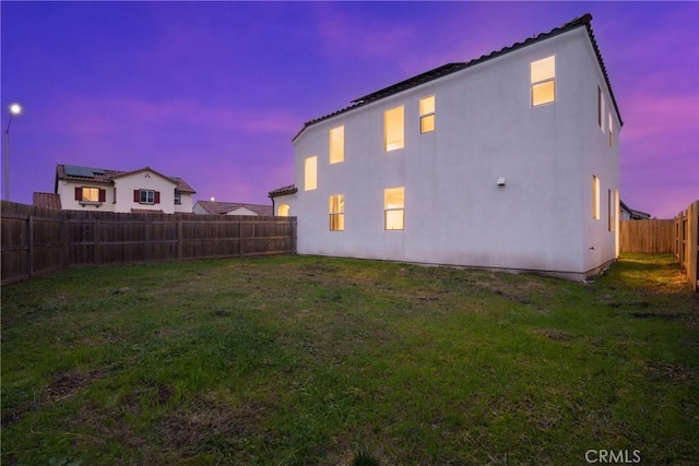 back of property at dusk featuring a fenced backyard, a lawn, and stucco siding